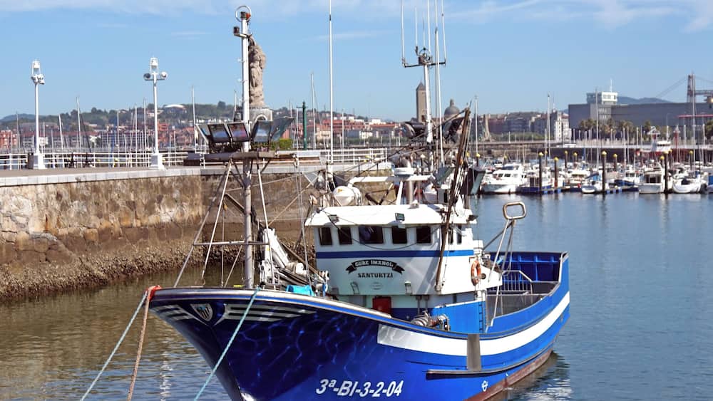 Un bateau de pêche bleu était amarré dans une marina, avec une vue sur la ville en arrière-plan.