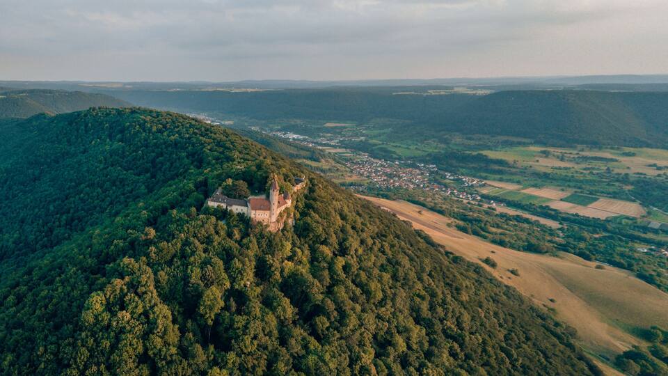 A castle on a hill overlooking a valley with scattered houses and fields.