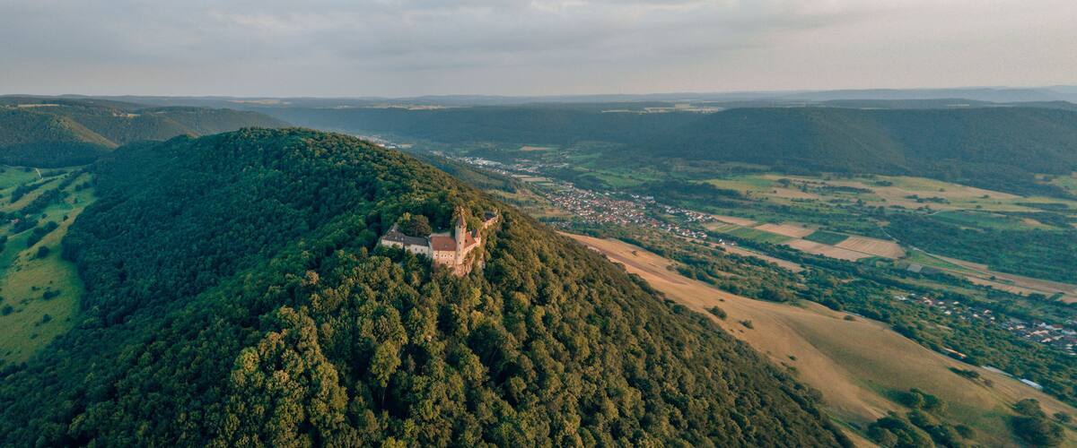 A castle on a hill overlooking a valley with scattered houses and fields.