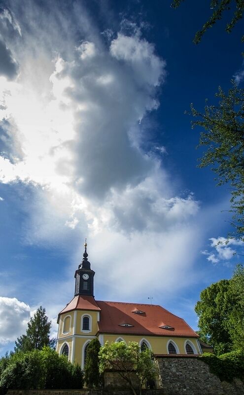 A church with a red roof and a clock tower under a partly cloudy sky.