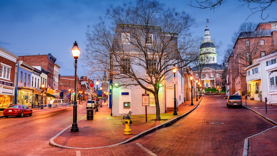 A historic town street at dusk with a prominent church dome, brick buildings, and a yellow fire hydrant.