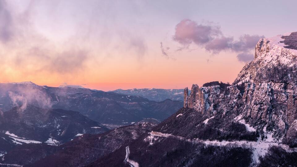 A mountainous landscape with snow-covered peaks and a sunset in the background.