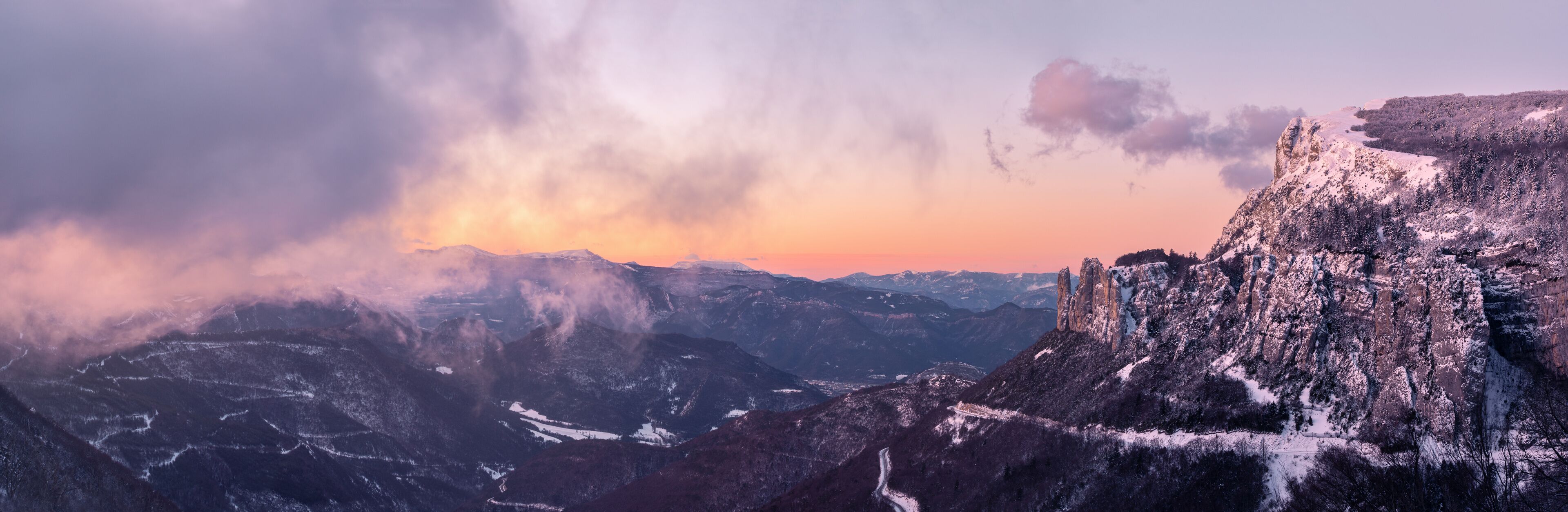 A mountainous landscape with snow-covered peaks and a sunset in the background.