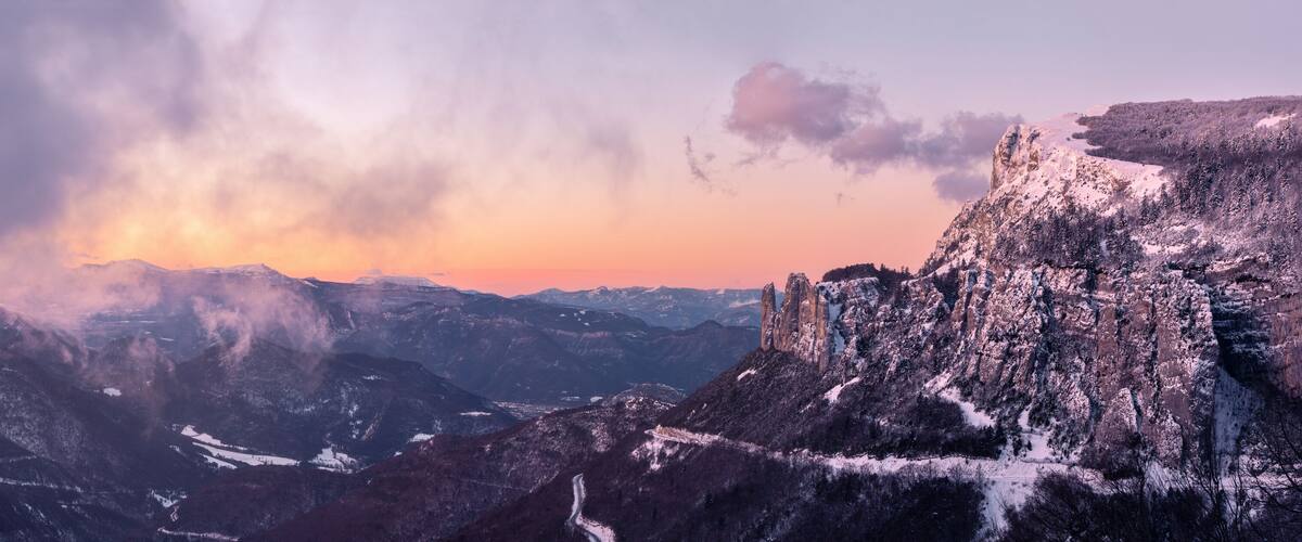 A mountainous landscape with snow-covered peaks and a sunset in the background.