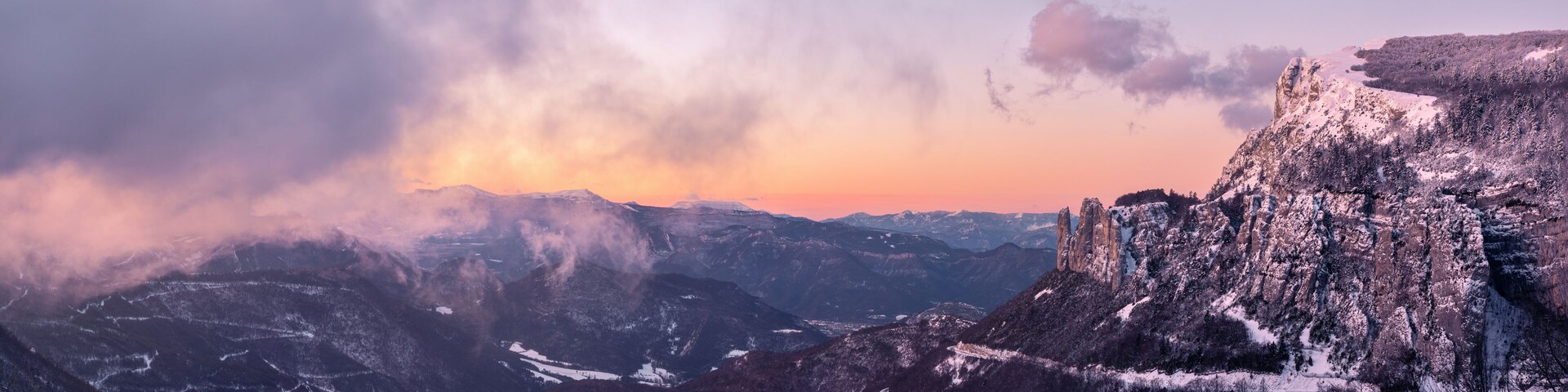A mountainous landscape with snow-covered peaks and a sunset in the background.