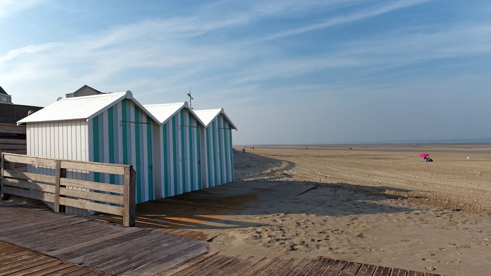 A wooden boardwalk leading to beach huts with striped awnings.