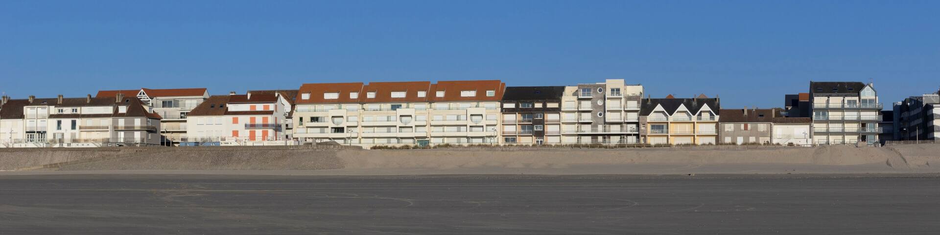 A coastal residential area with multi-story buildings, a sandy beach, and a clear blue sky.