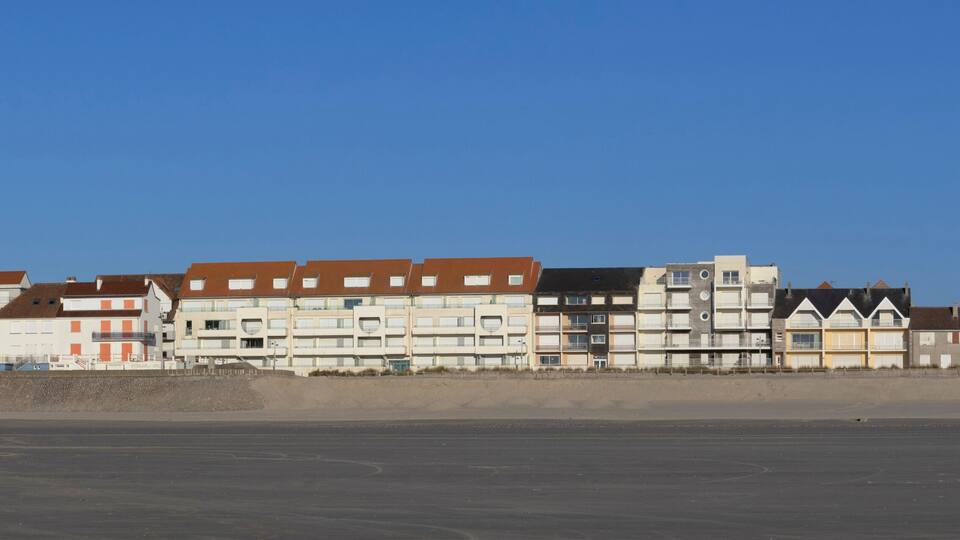 A coastal residential area with multi-story buildings, a sandy beach, and a clear blue sky.