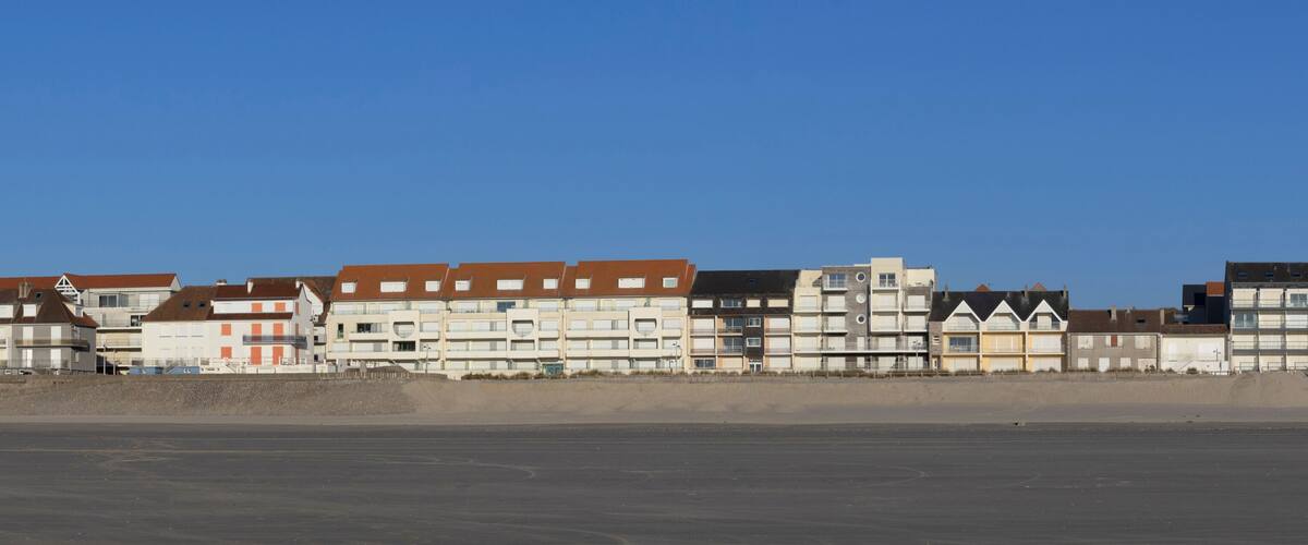 A coastal residential area with multi-story buildings, a sandy beach, and a clear blue sky.