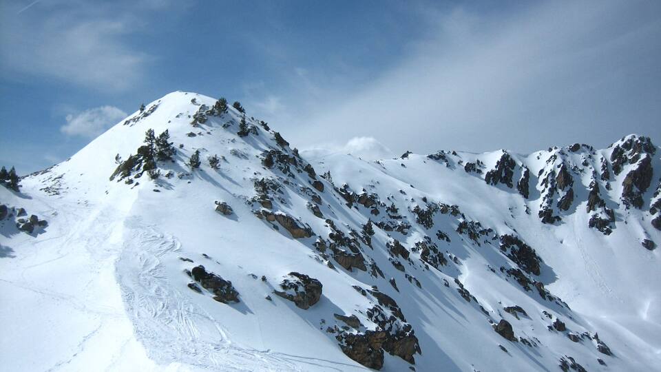 A snow-covered mountain with rocky outcrops and a clear blue sky.