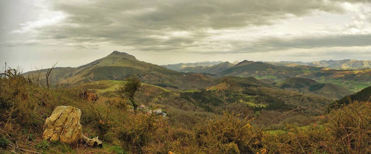 A mountainous landscape with rolling hills, a prominent peak, and a cloudy sky.