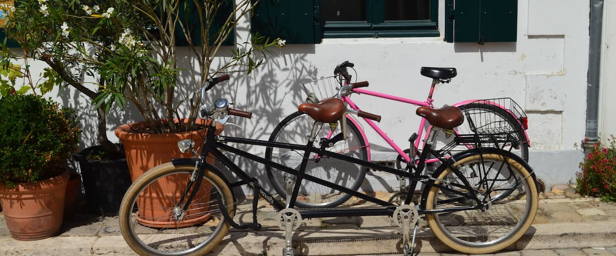 A black bicycle with pink accents parked next to a white building with green shutters.