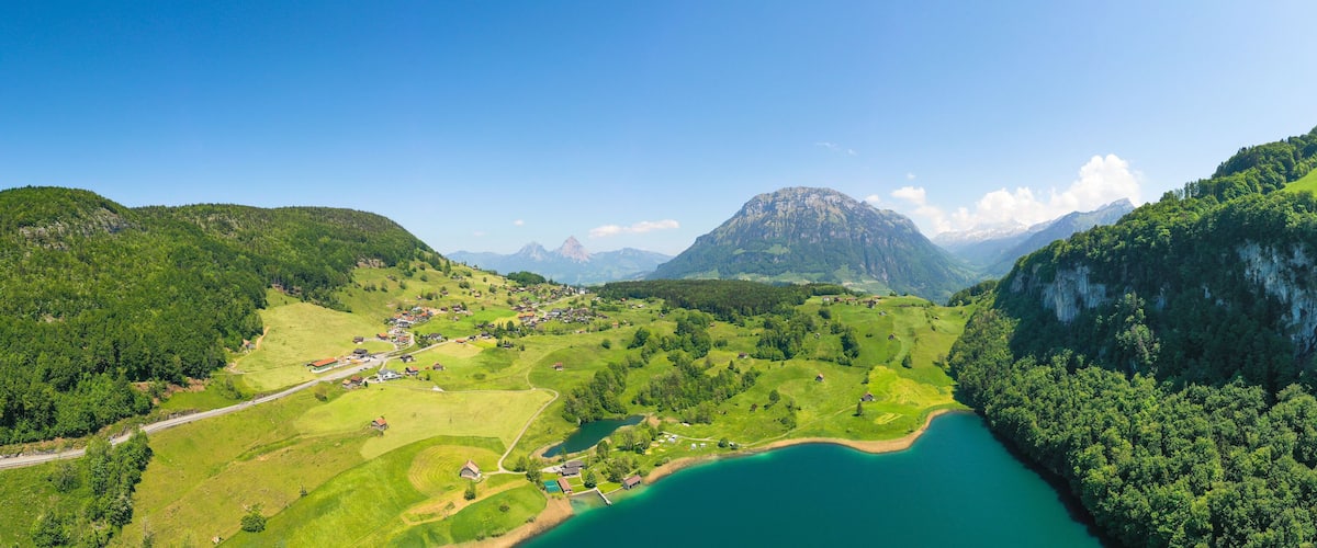A valley with a lake, surrounded by green hills and mountains.
