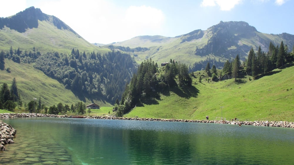 A clear mountain lake surrounded by lush green hills and dense forests.