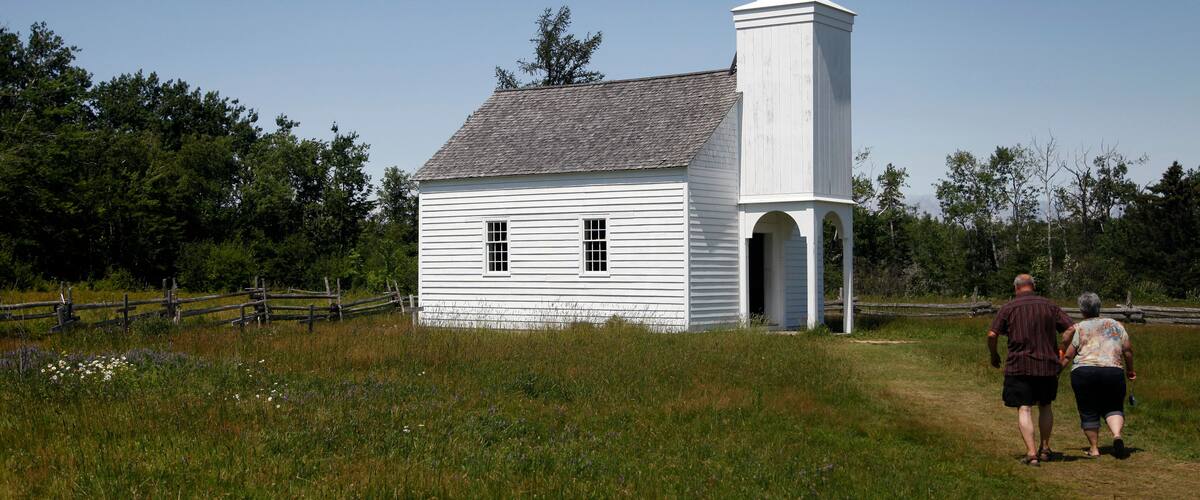 A white church with a bell tower and a fence in a grassy field.