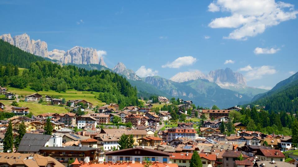 A mountainous village with traditional houses, green hills, and towering peaks in the background.