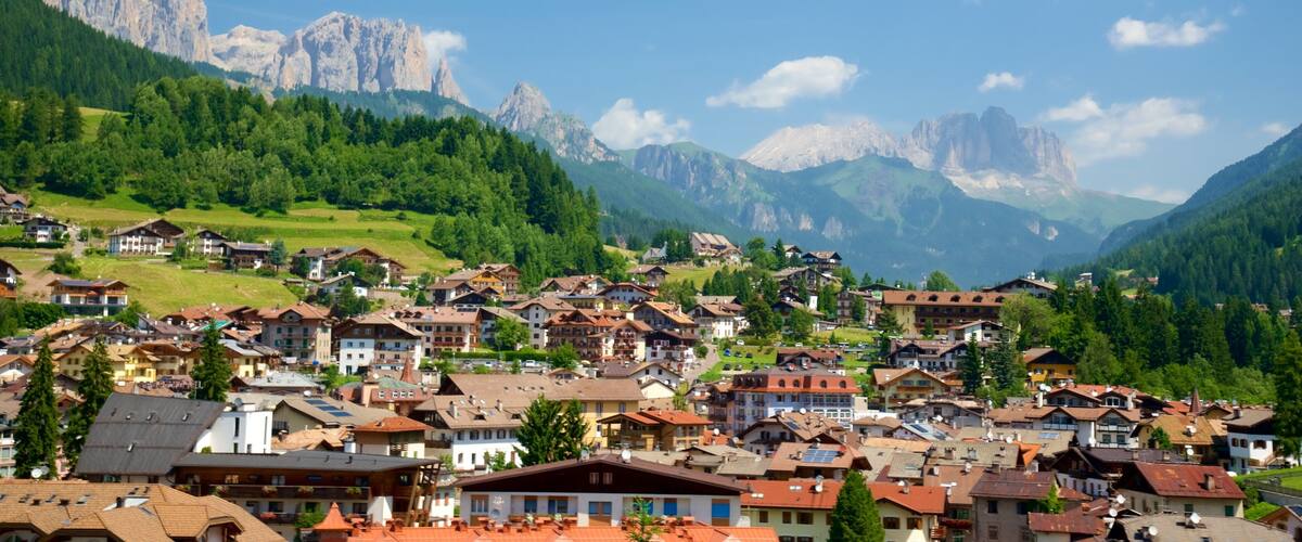 A mountainous village with traditional houses, green hills, and towering peaks in the background.