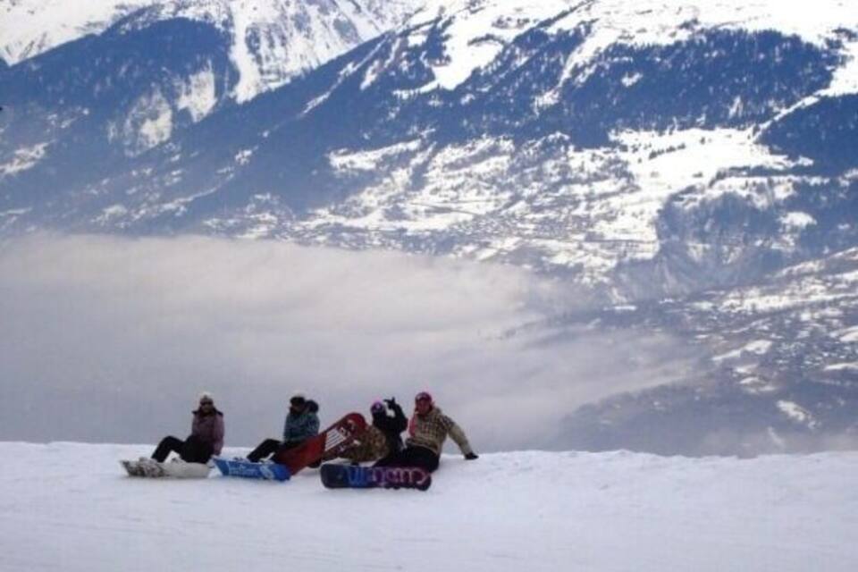 A group of people snowboarding on a snowy slope with mountains in the background.