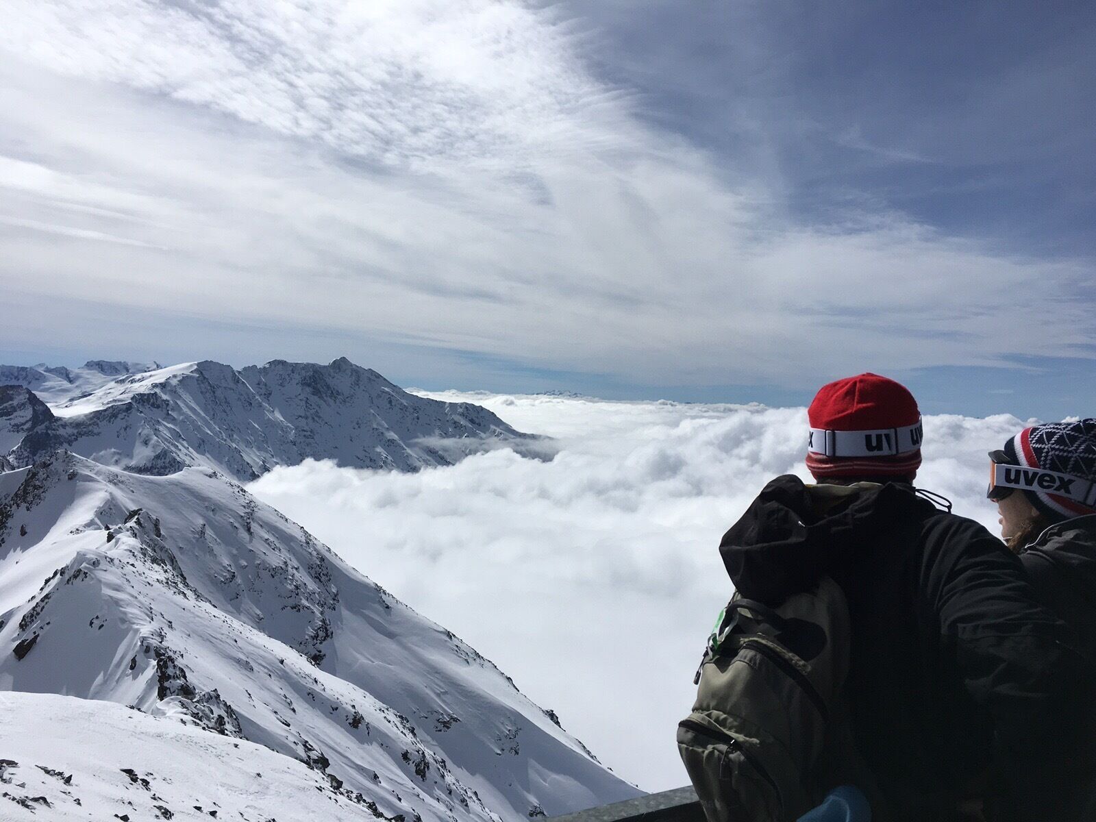 Two people on a snowy mountain peak overlooking a valley of clouds.