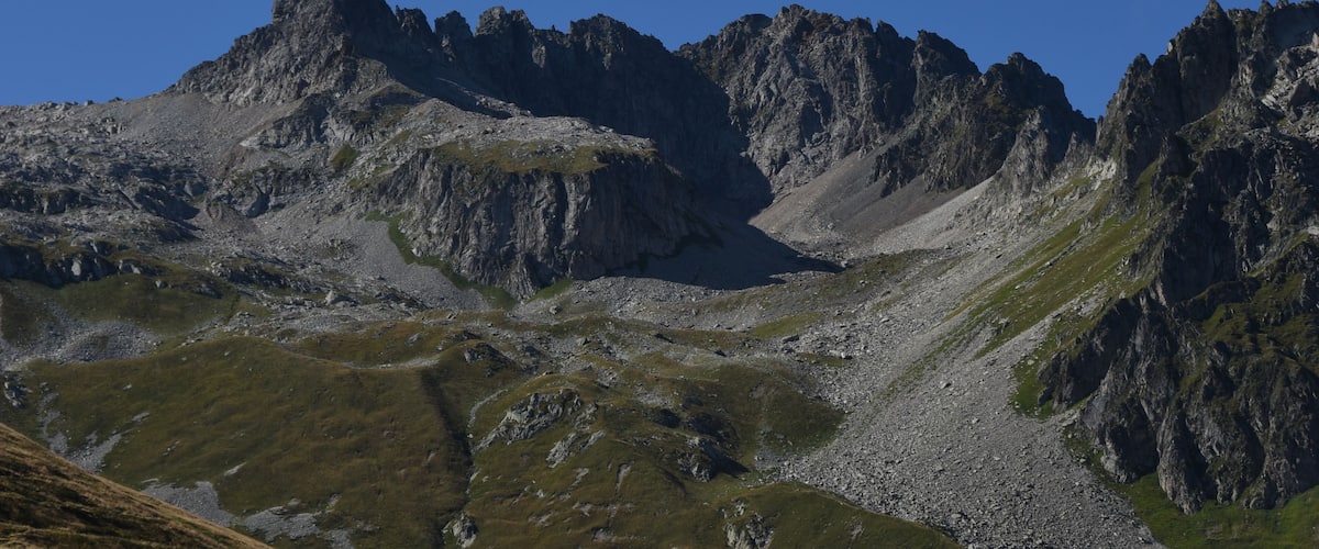 Rugged mountain peaks with sparse vegetation under a clear blue sky.