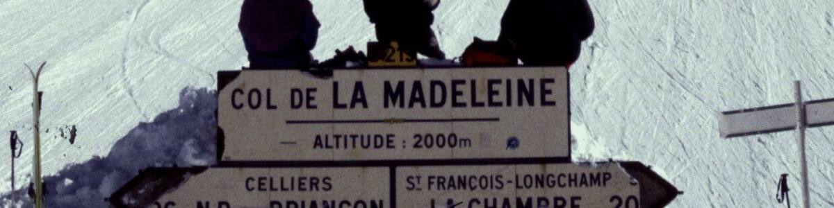 Une pente enneigée en montagne, avec des skieurs. Un panneau indique « COL DE LA MADELEINE » et précise que l’altitude est de 2 000 mètres.