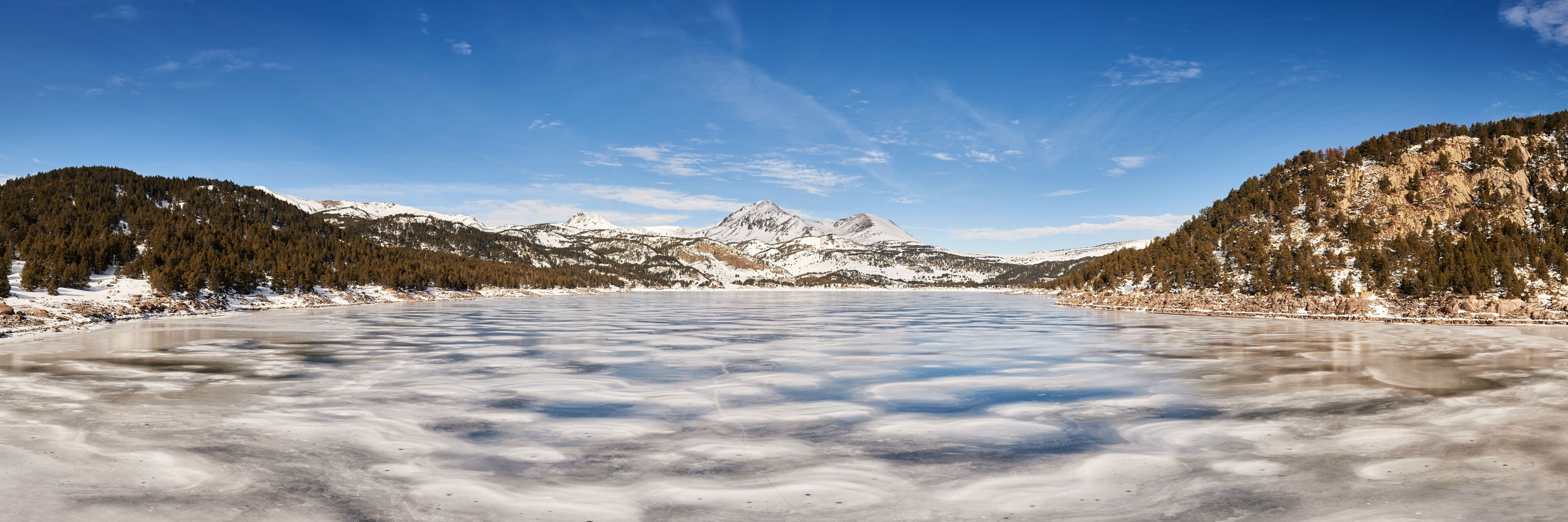 A frozen lake surrounded by snow-covered mountains and dense forests.