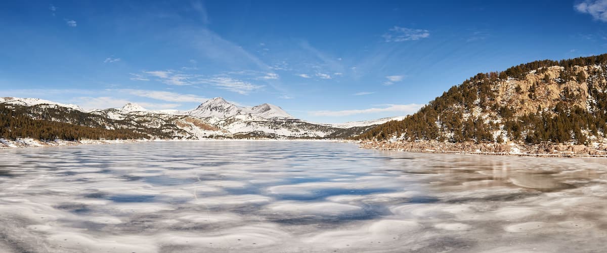 A frozen lake surrounded by snow-covered mountains and dense forests.