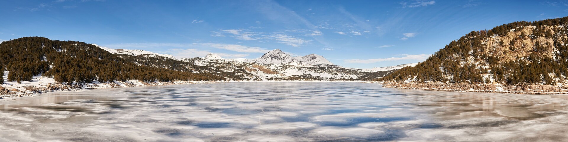 A frozen lake surrounded by snow-covered mountains and dense forests.