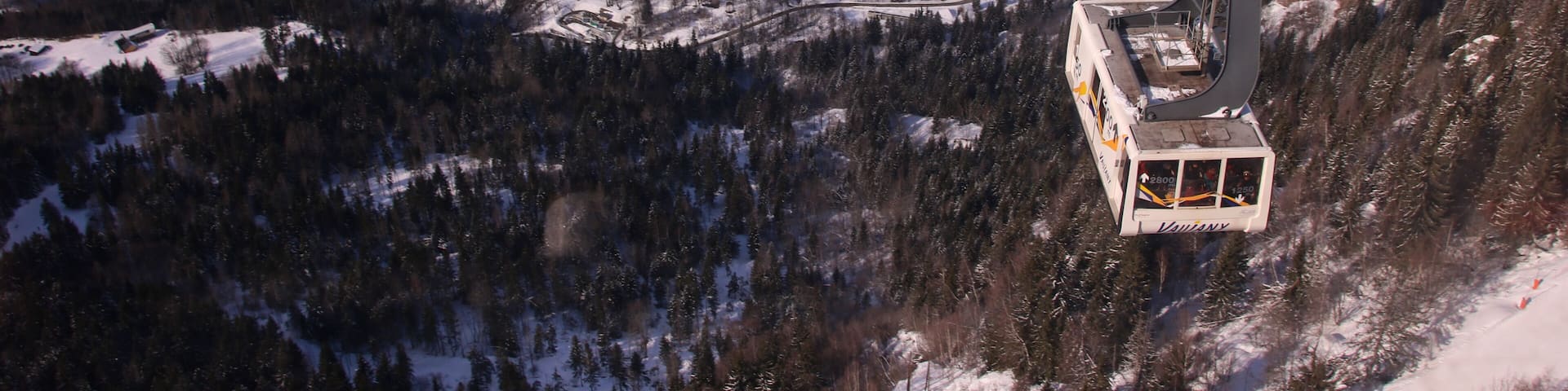 A cable car system in a snowy mountainous area with a village below.