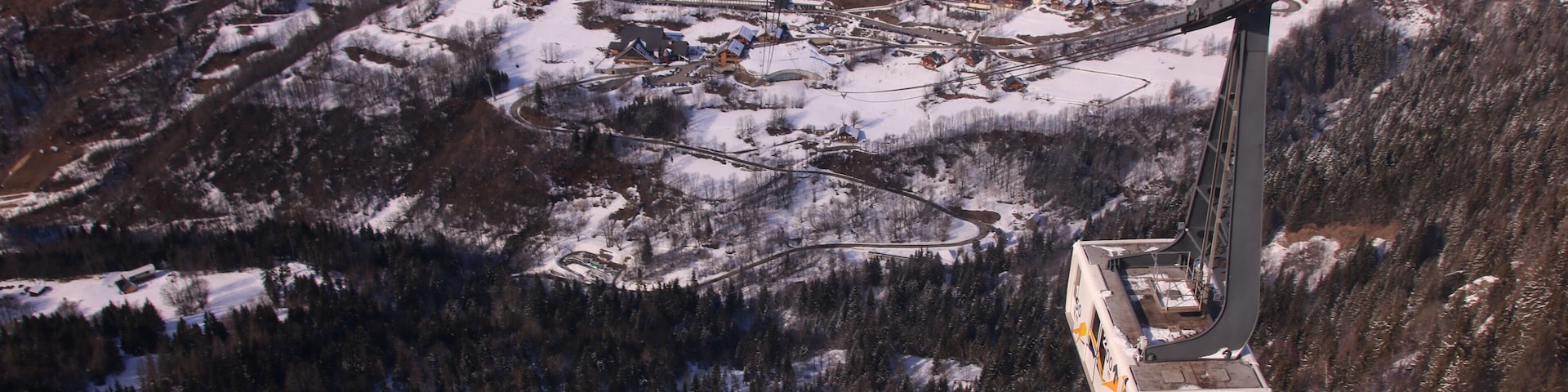 Sistema de teleférico en una zona montañosa nevada, con un pueblo en la parte baja.