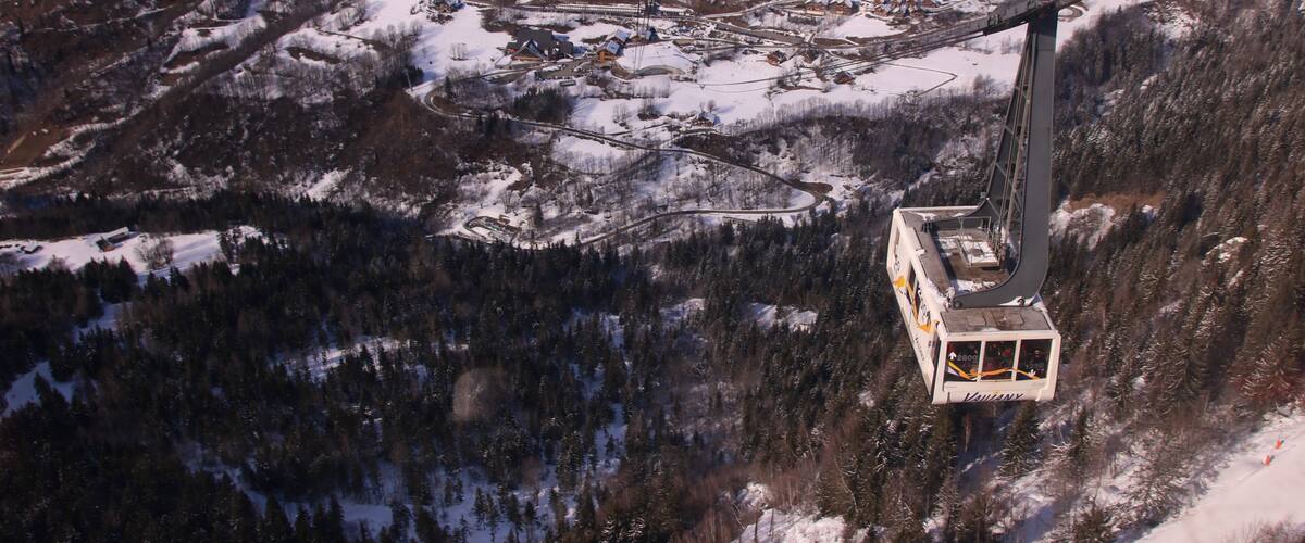 A cable car system in a snowy mountainous area with a village below.