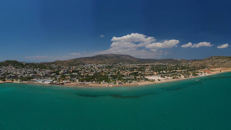 A coastal city with a beach, clear turquoise waters, and a mountainous backdrop.