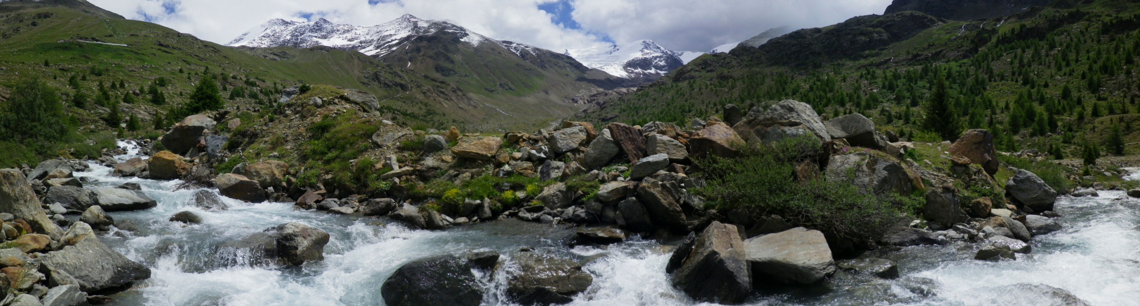 panoramic photo of mountain landscape in Valtellina, river Viola descends from the mountains in spring, Santa Caterina Valfurva, Lombardy, Italy