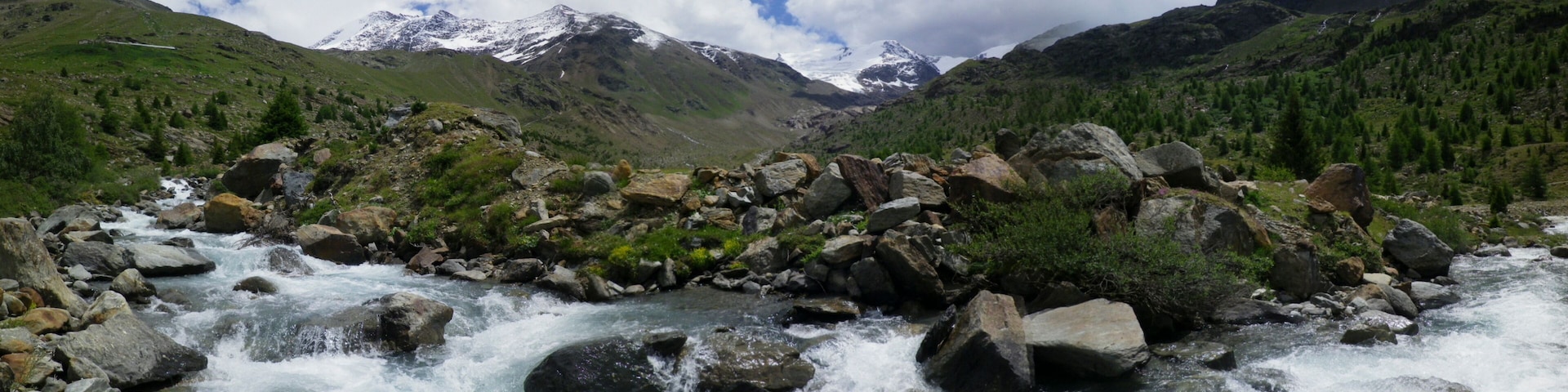 Un río fluye por un paisaje rocoso con montañas nevadas al fondo.