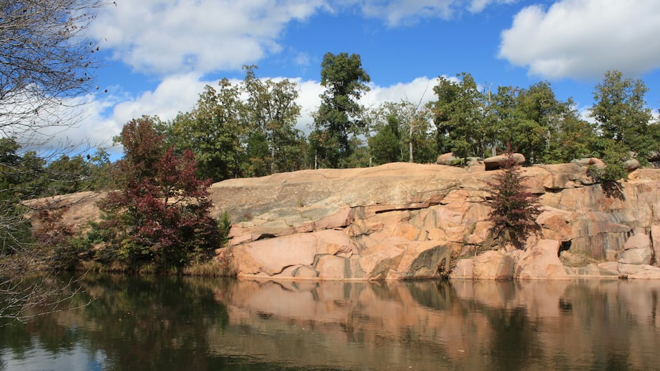 A rocky landscape with a calm lake reflecting the sky and trees.