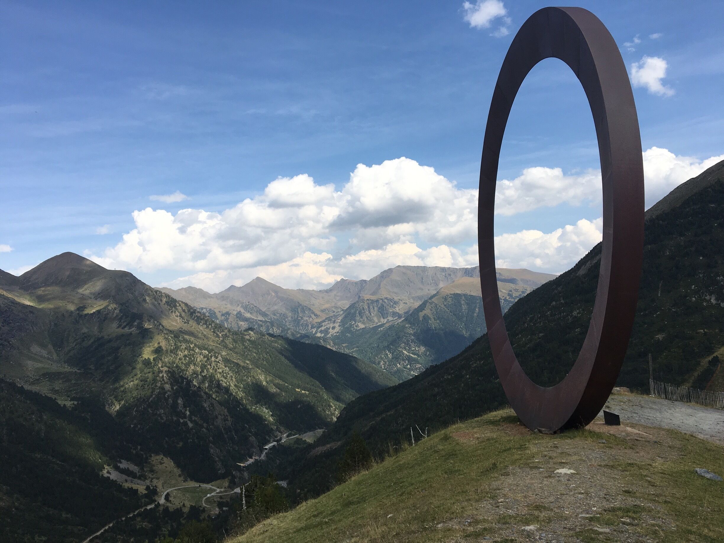 A large metal ring sculpture in a mountainous landscape with a clear sky.
