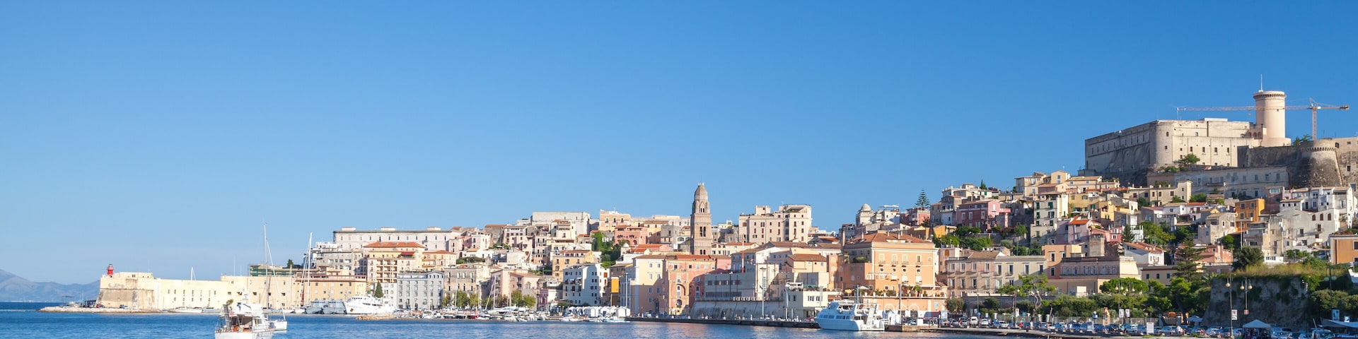 A coastal cityscape with historic buildings, a prominent tower, and boats in the harbor.