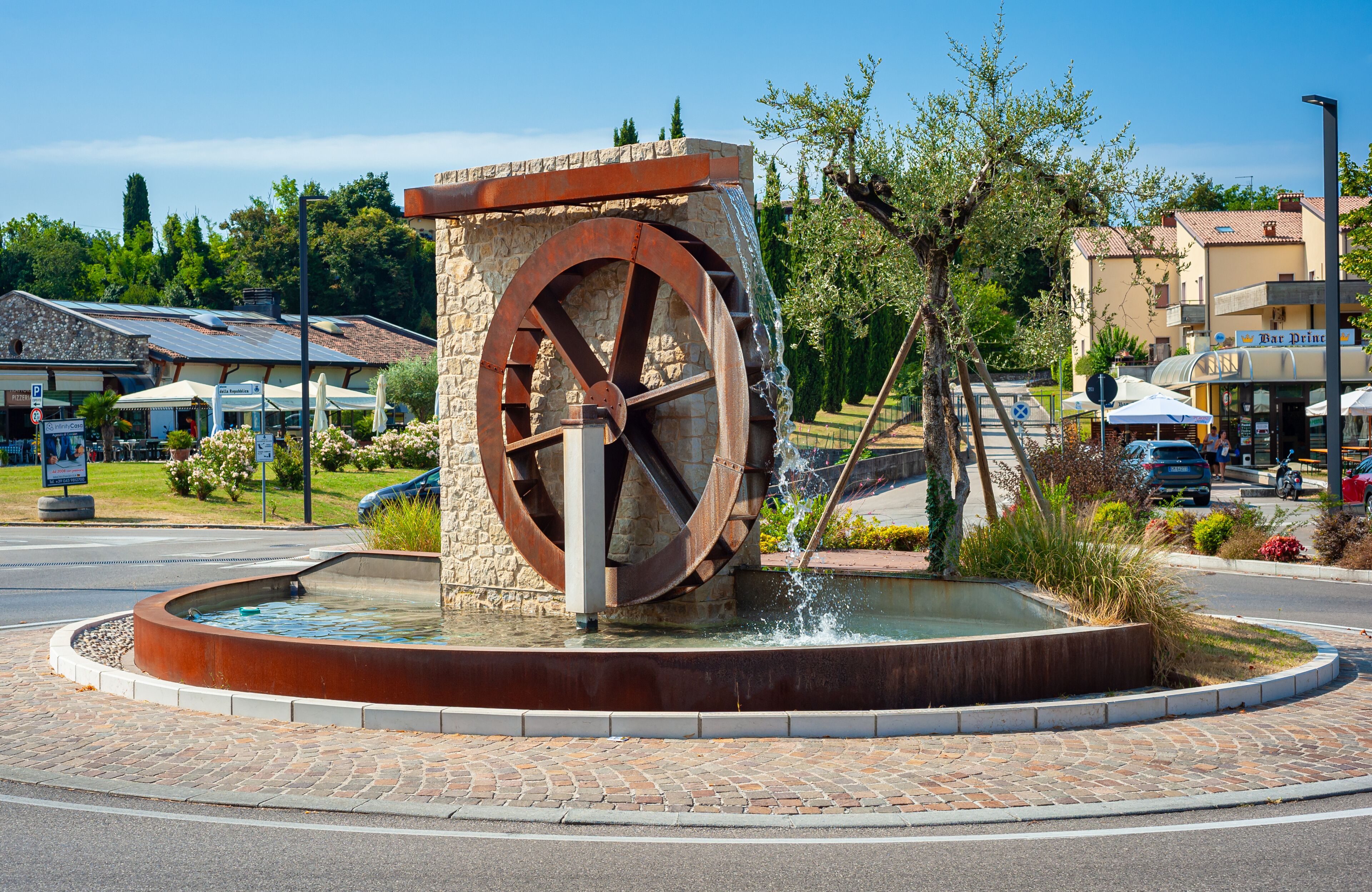 Costermano sul Garda, Italy - July 27, 2024: Beautiful view of water flowing through a spinning water wheel at a traffic circle in the village of Costermano sul Garda.