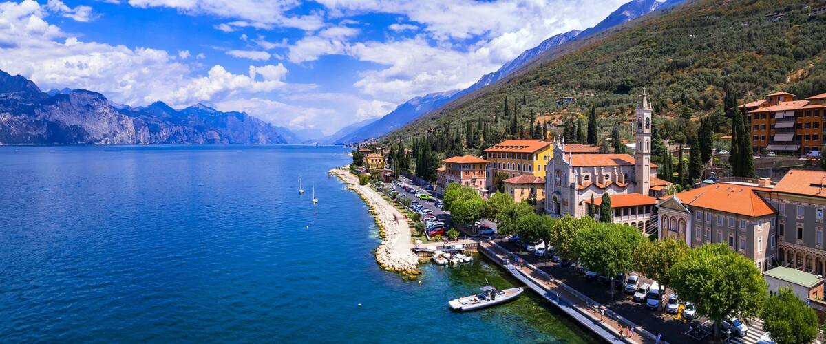 A coastal town with a marina, buildings with red roofs, and mountains in the background.