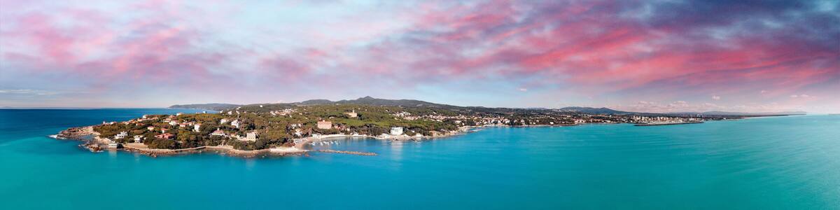 Une ville côtière offrant une vue dégagée sur la mer, avec une montagne imposante en arrière-plan et un ciel aux couleurs vives.