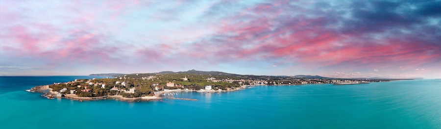 A coastal town with a clear view of the sea, a prominent mountain in the background, and a colorful sky.