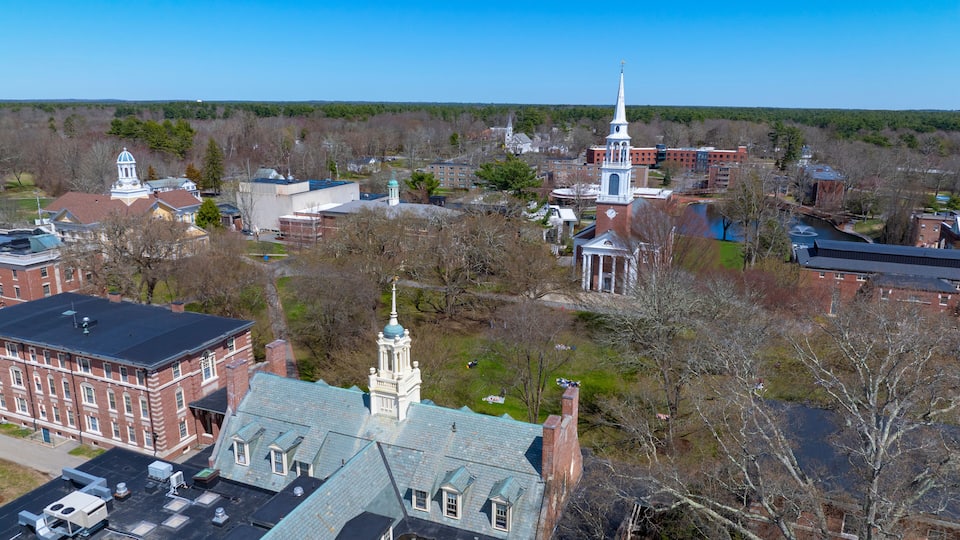 An aerial view of a university campus with historic buildings, a river, and surrounding greenery.