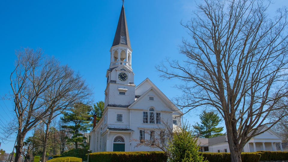 A white church with a steeple and clock tower, surrounded by trees and a well-maintained lawn.