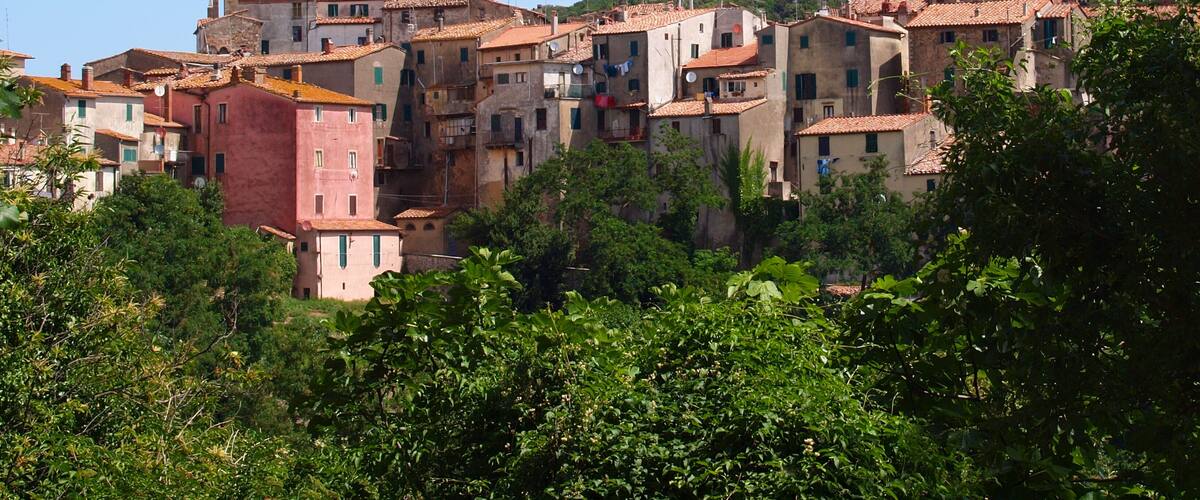A densely packed hillside village with terracotta-roofed buildings, surrounded by lush greenery.