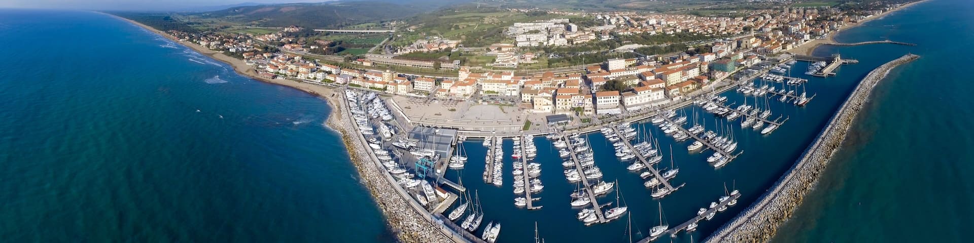 An aerial view of a coastal town with a marina, buildings, and surrounding hills.