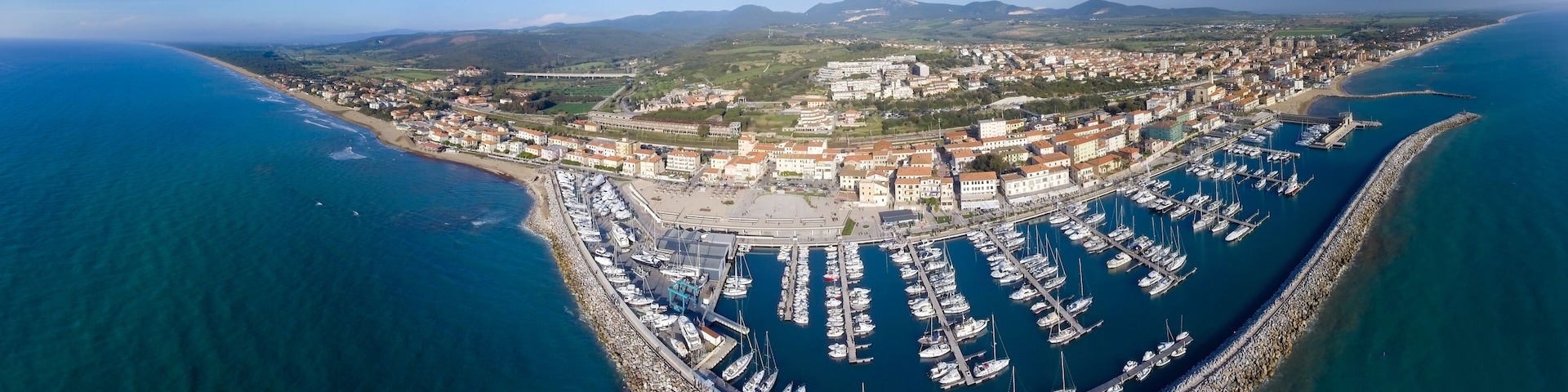 An aerial view of a coastal town with a marina, buildings, and surrounding hills.