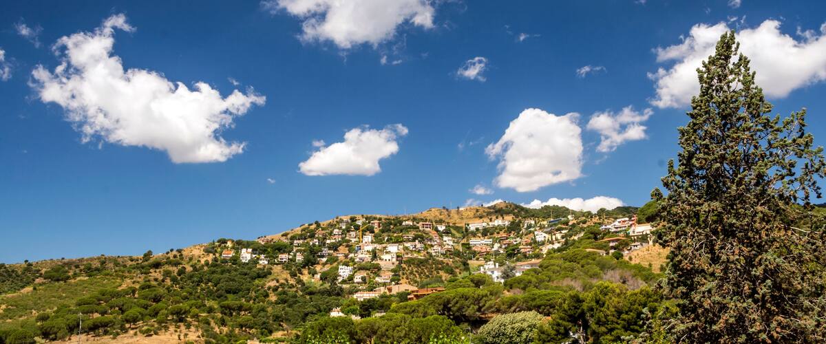 A hillside town with houses and trees under a blue sky with clouds.