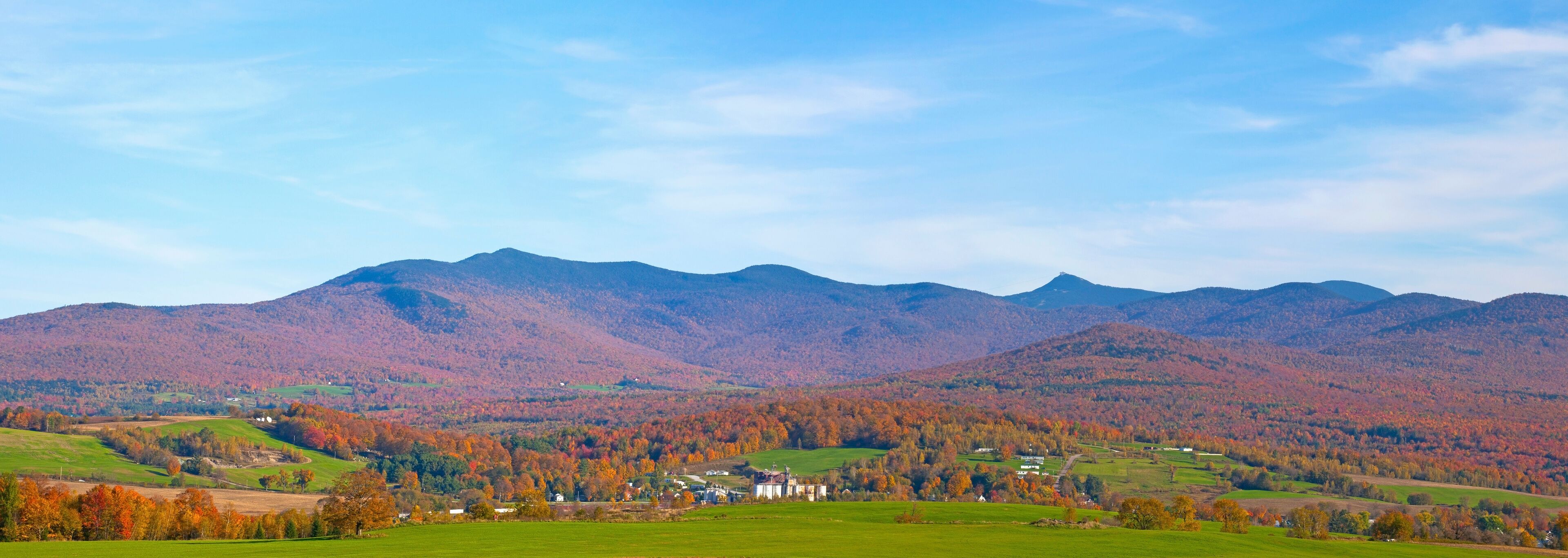 A mountainous landscape with autumn foliage, a green valley, and a white building in the foreground.