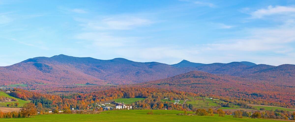 A mountainous landscape with autumn foliage, a green valley, and a white building in the foreground.