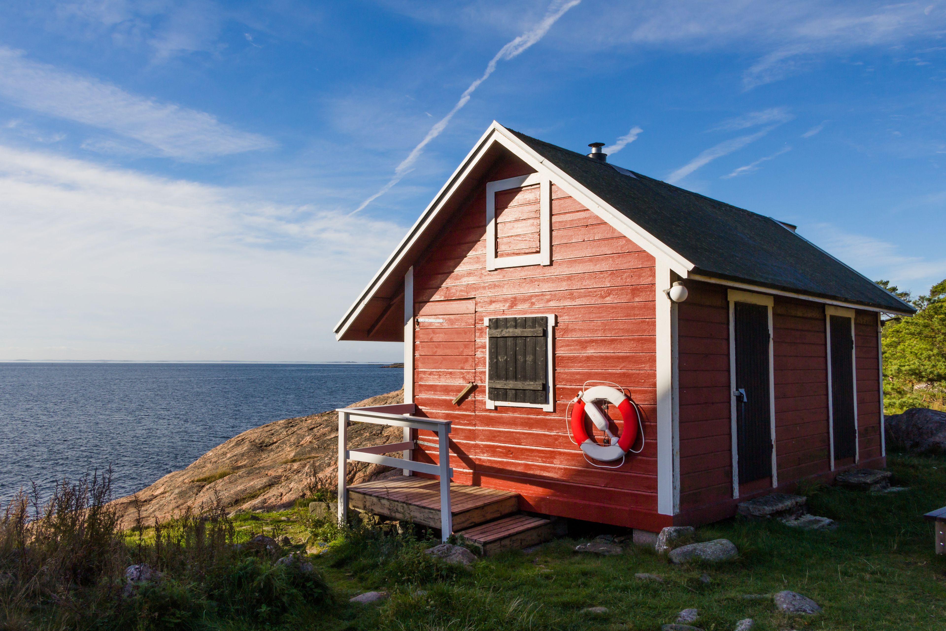 Eine rote Holzhütte mit weißer Tür, einem kleinen Fenster und einem Rettungsring, der an der Wand befestigt ist.